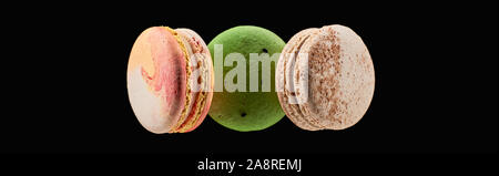 top view of three delicious colorful French macaroons of different flavors isolated on black, panoramic shot Stock Photo