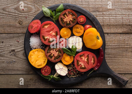 top view of tomatoes, garlic, spinach, chilli pepper, salt and pepper on pizza pan on wooden table Stock Photo