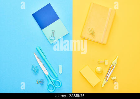Top view of yellow and blue notepads with different stationery on bicolor background Stock Photo
