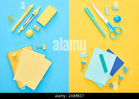 Top view of different colorful stationery with yellow and blue notepads on bicolor background Stock Photo