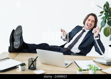 happy businessman talking on telephone, holding smartphone and headset in hands Stock Photo