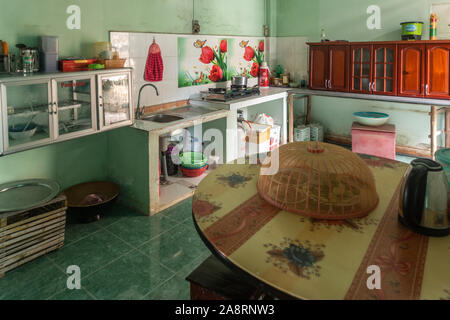 Nha Trang, Vietnam - March 11, 2019: Inside Farm house. Kitchen with sink, stove, reddish cabinets and table. Pots and pans. Green wall. Stock Photo