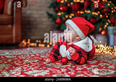 Little six month old baby dressed as Santa Claus. Background for christmas card. The child looks up at the place for inscription on background of lumi Stock Photo