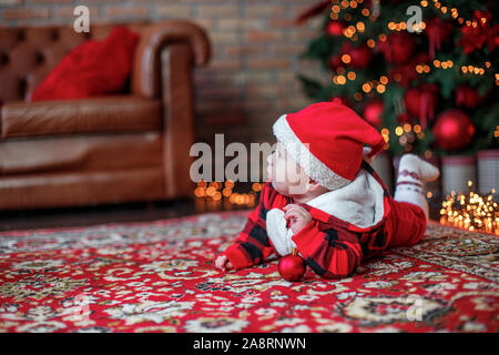 Little six month old baby dressed as Santa Claus. Background for christmas card. The child looks up at the place for inscription on background of lumi Stock Photo