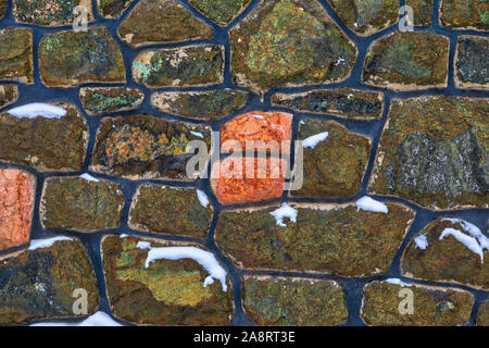 Detail of an colorful frozen stonewall partially covered with snow. Image Stock Photo