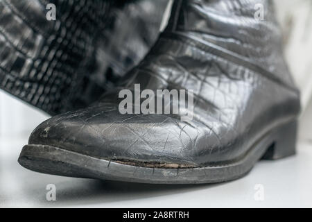 Old women's boots with side damage made of genuine leather imitating a crocodile pattern. Stock Photo