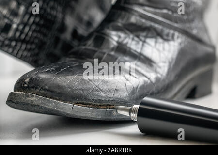 Old women's boots with side damage made of genuine leather imitating a crocodile pattern and a tube with glue for self-repair at home. Stock Photo