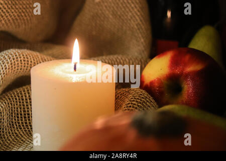 Warm autumn still life. White candle soft light and apple with drops of water on it on sackcloth background. Close up. Stock Photo