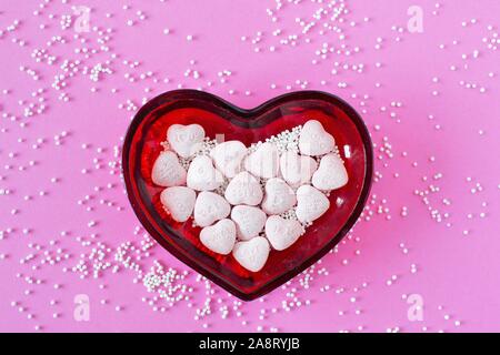 Valentine candy hearts and sprinkles in a heart-shaped dish. Stock Photo