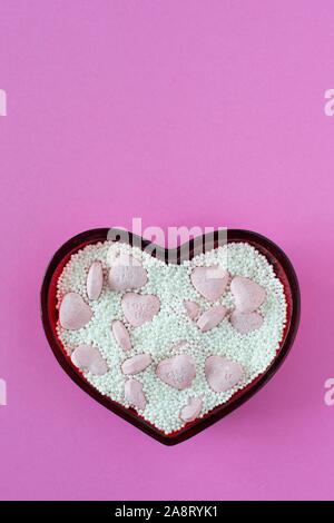 Valentine candy hearts and sprinkles in a heart-shaped dish. Stock Photo