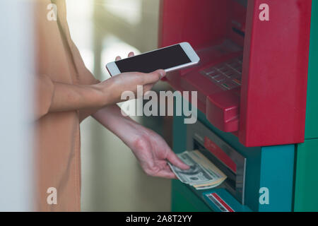 woman using the smart mobile phone for withdrawing in front of the ATM, business Automatic Teller Machine concept Stock Photo