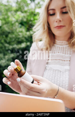 Pensive business lady reading instructions on bottle with cosmetic oil, selective focus Stock Photo