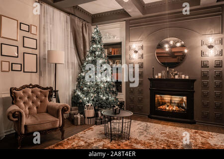 Christmas evening by candlelight. classic apartments with a fireplace, decorated tree, sofa, large windows and chandelier. Stock Photo