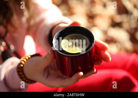 Children's hands hold a red mug with tea in the autumn park Stock Photo