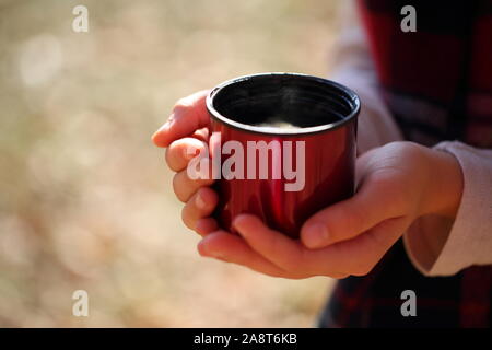 Children's hands hold a red mug with tea in the autumn park Stock Photo
