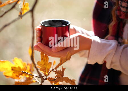 Children's hands hold a red mug with tea in the autumn park Stock Photo