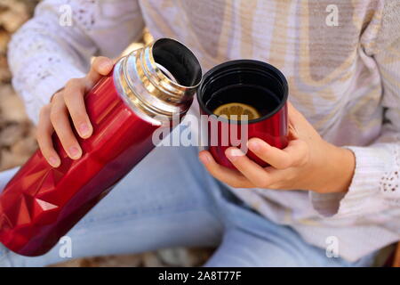Children's hands hold a red mug with tea in the autumn park Stock Photo