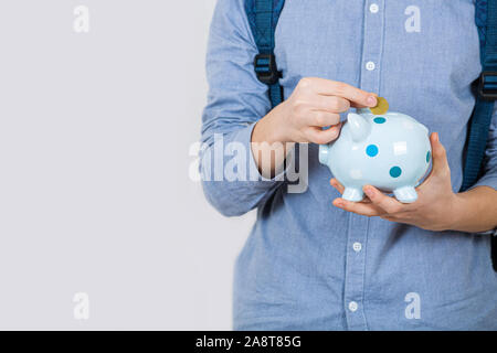 Teenager boy holding piggy bank putting euro coins inside over white background. Financial education savings concept. Stock Photo