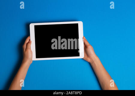 Kid hands holding white tablet computer on light blue background Stock Photo