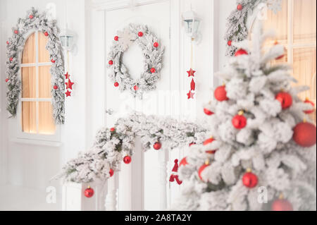 merry christmas decoration on white house home porch with wreath on door and Xmas tree with toys and window with warm light inside Stock Photo