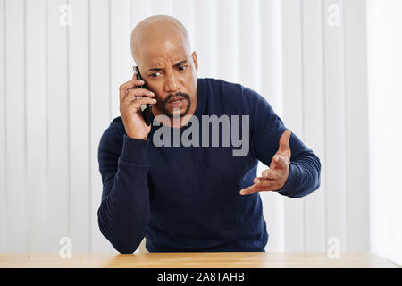 Frowning unhappy entrepreneur talking on phone and arguing with business partner Stock Photo