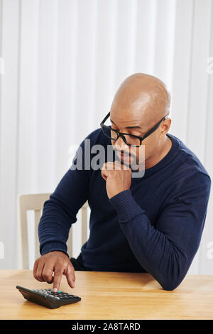 Businessman in glasses counting something on calculator when sitting at office desk Stock Photo
