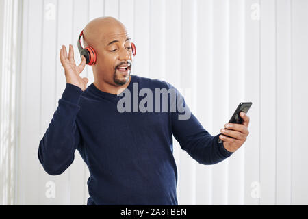 Happy mature man in headphones dancing and listening to music on his laptop Stock Photo