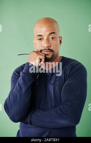 Pensive tired muscular man with circle beard taking off glasses and looking at camera Stock Photo