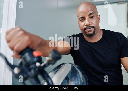Portrait of handsome muscular man in black t-shirt sitting on motorcycle and looking at camera Stock Photo