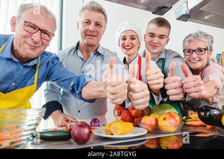 Trainees and their nutritionist in a training kitchen showing thumbs Stock Photo