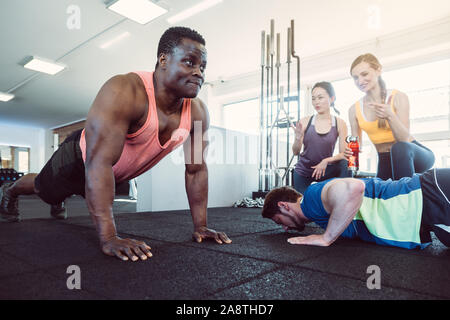 Two men have a push-up competition in the gym with girls cheering Stock Photo