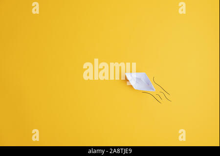 White paper made origami boat on yellow surface with hand drawn waves behind it. With copy space ready for your message or text. Stock Photo