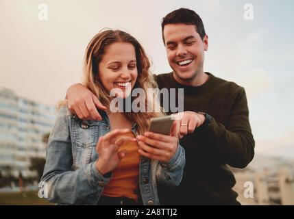 Smiling young group of friends using mobile device apps, surfing internet at outdoors Stock Photo