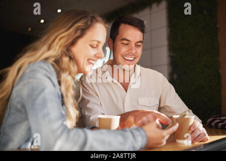 Happy young friends sitting together in coffee shop using smartphone - smiling modern real people Stock Photo