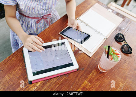 Hands of young woman checking calendar on her tablet computer and reading travel packing checklist Stock Photo