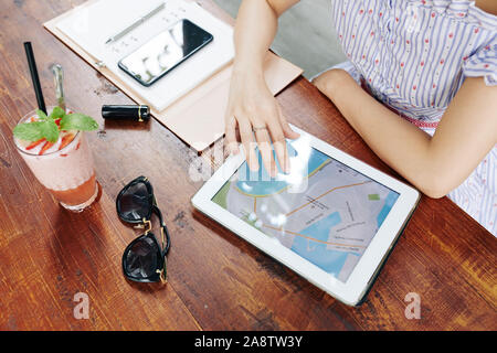 Hands of young woman drinking strawberry milkshake when using map application on tablet computer when planning vacation Stock Photo