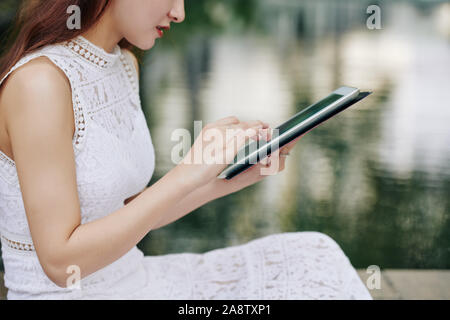Cropped image of young woman working on digital tablet when sitting at small pond in city park Stock Photo