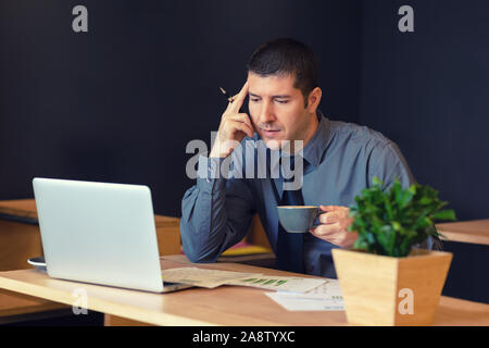 Thoughtful businessman sitting at table in trendy cafe remote working on laptop Stock Photo