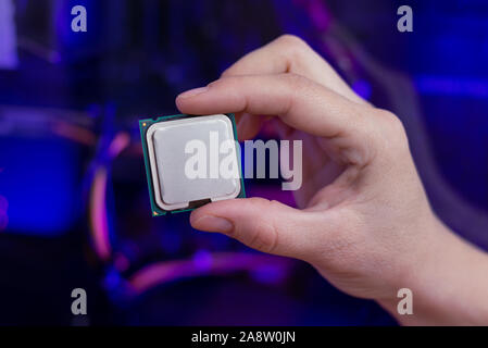 Hand holds a modern processor. Computer with RGB illumination in background. Close-up. Stock Photo
