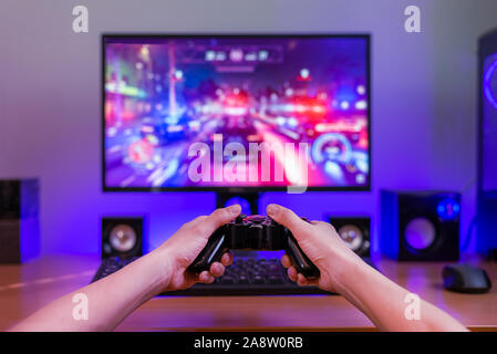 Joypad in hands. Computer gaming concept. Computer display with game in background. RGB light behind the desk. Stock Photo