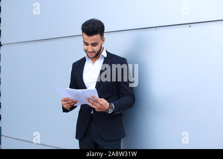 Arabian Successful businessman holds documents, smiling little smile and thinks near wall of business center. Stock Photo