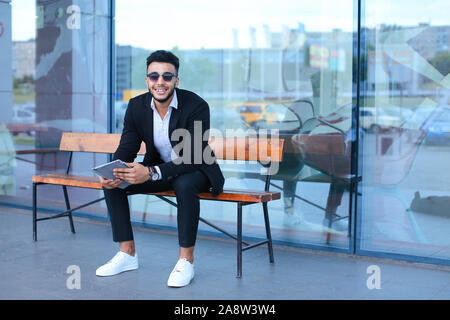 Man in suit arabic puts on sunglasses with tablet near business center Stock Photo