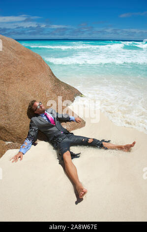 Castaway survivor businessman washed up on a tropical beach in a ragged torn suit Stock Photo