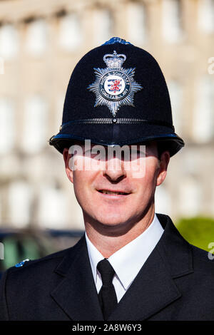 A close up head shot of a British Police Officer, or Bobby, in full dress uniform wearing a traditional custodian helmet Stock Photo