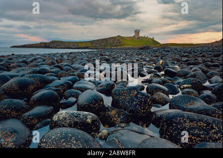 Dunstanburgh castle from the boulders on the shore of  Embleton Bay on the Northumberland coast. Stock Photo