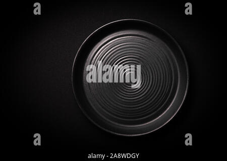Closeup empty round black ceramic plate with pattern of circles on dark background with copy space. Overhead view. Concept modern shooting menu from c Stock Photo