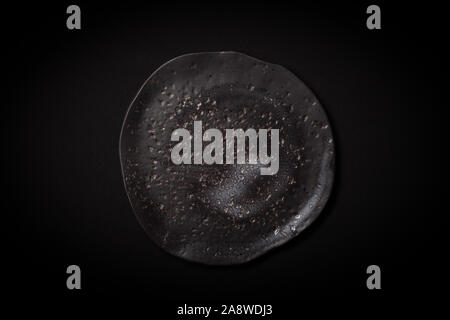 Closeup empty round black aged ceramic plate on dark background with copy space. Overhead view. Concept modern shooting menu from chef, restaurant adv Stock Photo