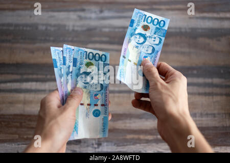 Hand holding cash banknote of one thousand Philippines peso paying bills, payment procedure or bribe, salary Stock Photo