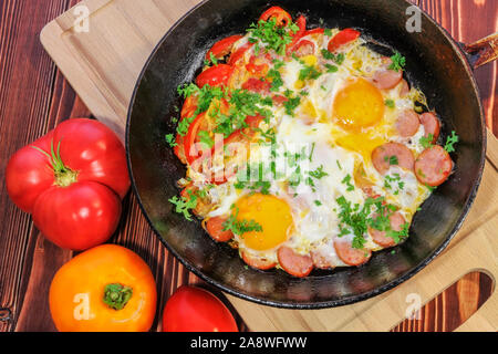 Scrambled eggs with tomatoes, sausages, sweet pepper and sprinkled with chopped parsley in a frying pan Stock Photo