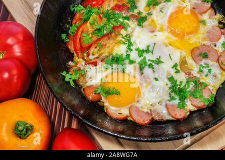 Scrambled eggs with tomatoes, sausages, sweet pepper and sprinkled with chopped parsley in a frying pan Stock Photo
